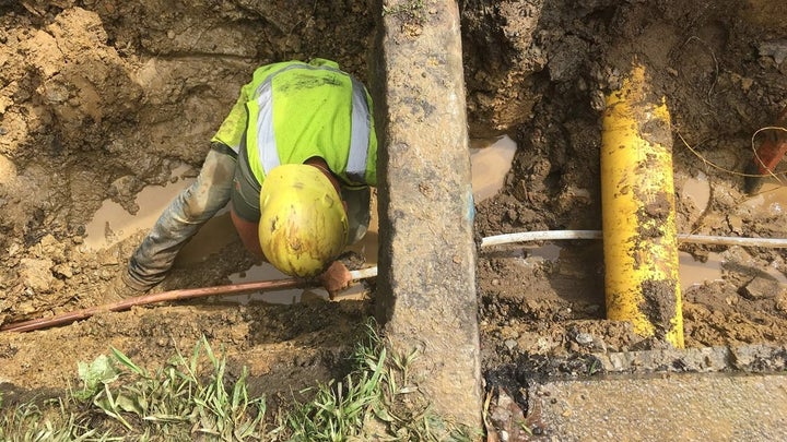 After digging out the road and lawn, a worker ducks under the curb while connecting a copper pipe on private property with a Pex tube on public property. 