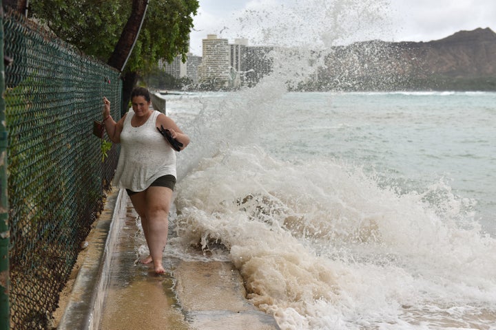A woman tries to walk on a seashore road while strong tides lapping the seawall at Waikiki Beach.