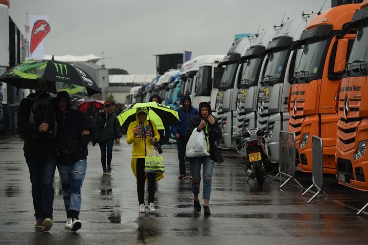 People shelter under umbrellas and raincoats as the start of the MotoGP race is delayed due to rain during the motorcycling British Grand Prix at Silverstone circuit in Northamptonshire today