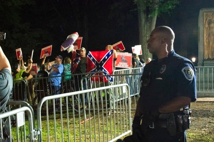 A police officer stands behind the barricades as "Silent Sam" supporters raise Confederate flags and posters that say, "Save our monuments."