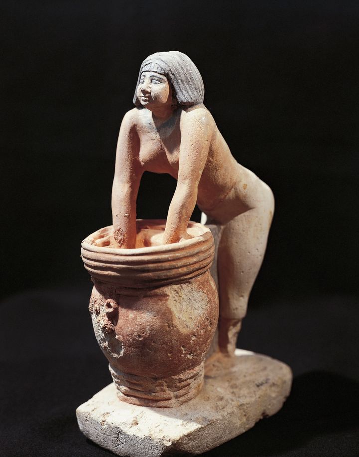 Circa 1900: A painted limestone statuette of a woman making beer in Egypt.