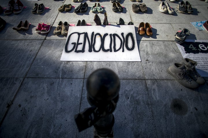 A sign that says "genocide" in Spanish is displayed next to empty shoes as part of the June 1, 2018, protest outside the Capi