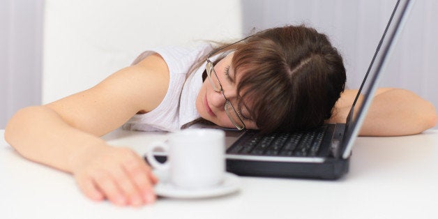 Young woman comically sleeps on laptop at office