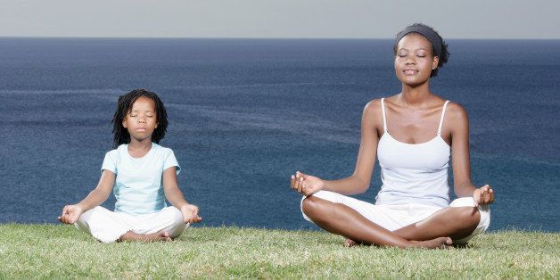 Mother and daughter (5-7) meditating on cliff top, eyes closed