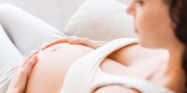 Close-up of pregnant young woman in white tank top touching her belly