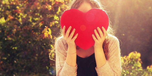 A girl holding up a heart in golden hour.