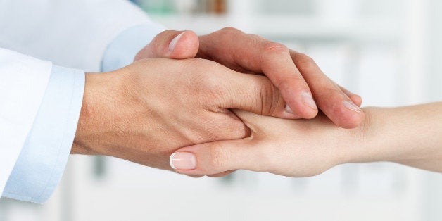 Friendly male doctor's hands holding female patient's hand for encouragement and empathy. Partnership, trust and medical ethics concept. Bad news lessening and support. Patient cheering and support