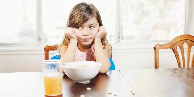 Girl (3-5) sitting at table with cereal, head in hands