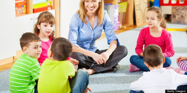 Preschool: Young smiling teacher discussing with group of children. Learning and having fun. Selective focus to teacher and cute little girl.