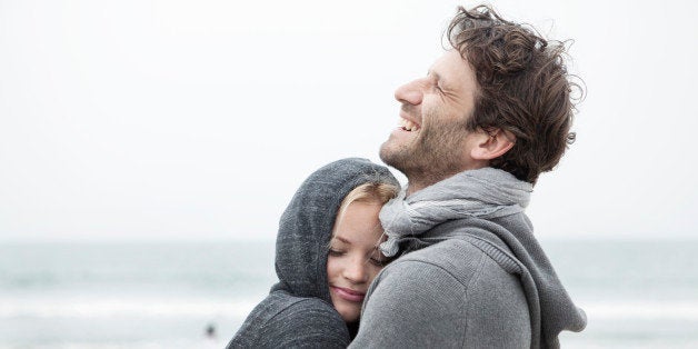 a beautiful young couple cuddle at the beach in a nice and lovely way. it looks like a great moment of love at the beach.