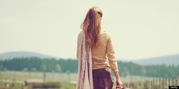 Woman walking on a country road with old suitcase