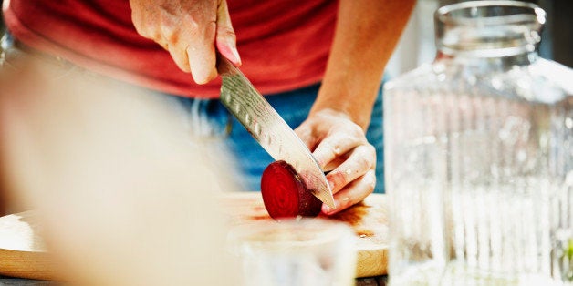 Woman slicing organic beet on cutting board at table on outdoor patio