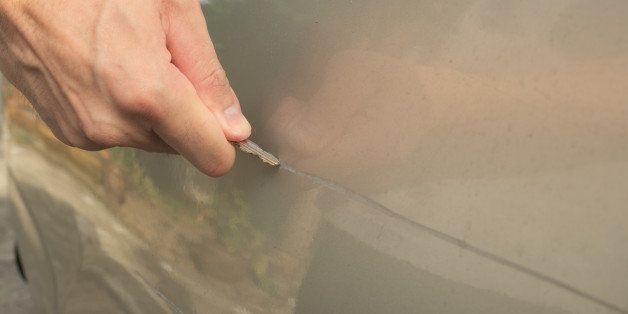 Male hand scratching a car by using silver key