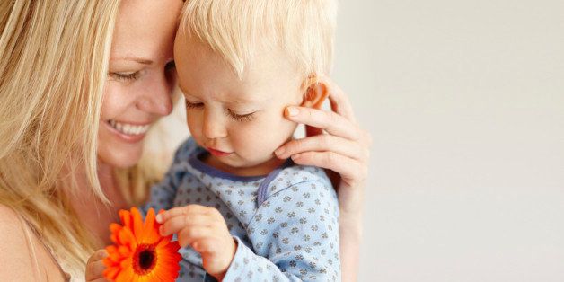 A loving mother holding her son as he looks at an orange flower