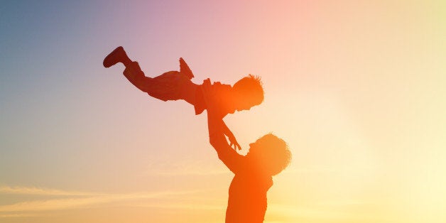 father and little son silhouettes play at sunset sky