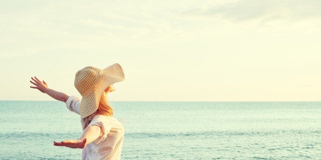 Happy beauty woman in hat is back opened his hands, relaxes and enjoys the sunset over the sea on the beach