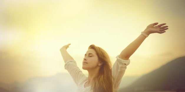 freedom concept, woman with arms raised in sunset field.