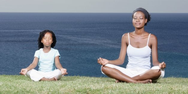 Mother and daughter (5-7) meditating on cliff top, eyes closed