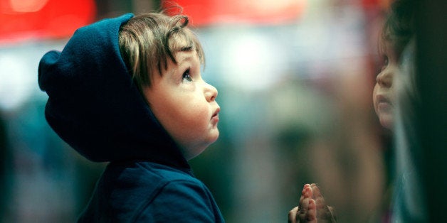 Boy watching storefront with his own reflection on it.