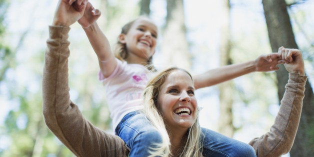 Mother carrying daughter on shoulders in woods