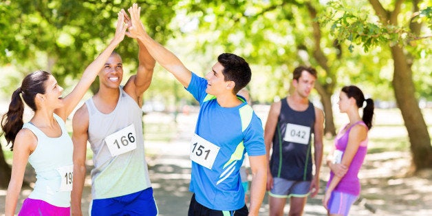 Happy multi-ethnic marathon runners giving high-five with people in background in park. Horizontal shot.