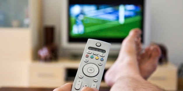 Close up of hand holding a remote control with flatscreen television showing sport in the background. Focus on the OK button.Please see some similar pictures from my portfolio: