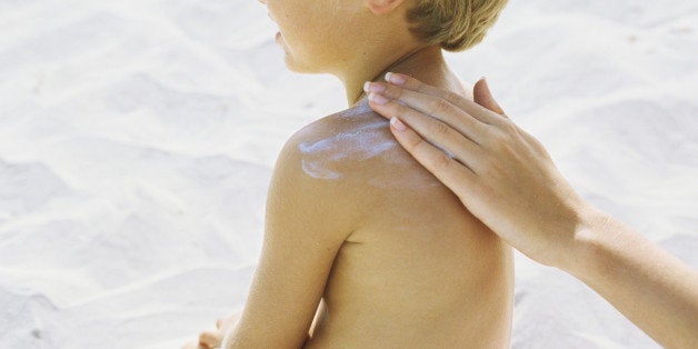 Little boy on beach having sunscreen rubbed into shoulder by mother