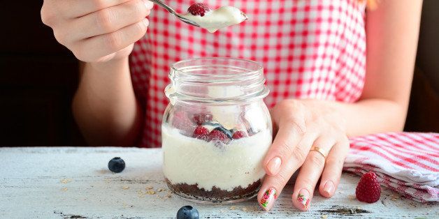 Redhead girl in red morning dress eating creamy dessert in jar with brownies and yogurt topped with fresh raspberries and blueberries, bright colorful image. Clean eating.