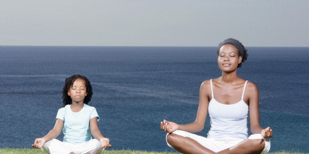 Mother and daughter (5-7) meditating on cliff top, eyes closed