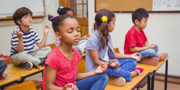 Pupils meditating in lotus position on desk in classroom at the elementary school