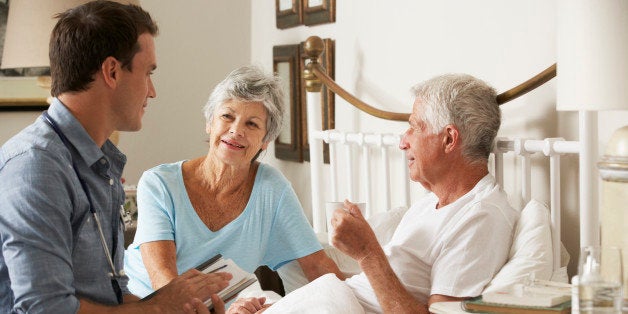 Doctor On Home Visit Discussing Health Of Senior Male Patient With Wife In Bedroom.