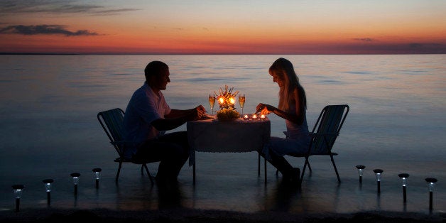 young couple share a romantic dinner with candles on the sea sand beach