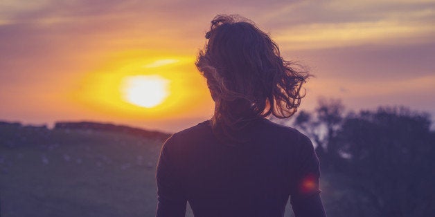 Rear view of young woman admiring the sunset over a field from her balcony