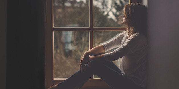 Young attractive woman, sitting on a window, looking outside, lonely mood