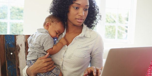 Mother With Baby Working In Office At Home Looking At Laptop