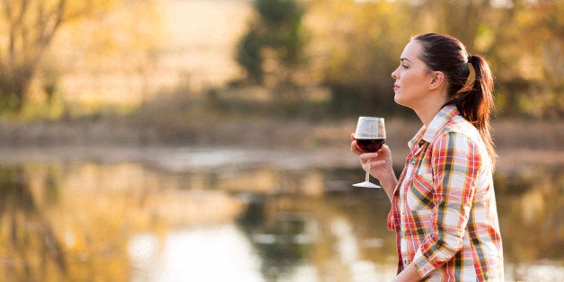 thoughtful young woman with glass of wine on pier in autumn