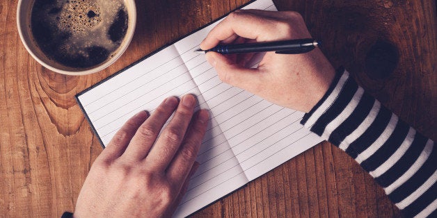 Woman drinking coffee and making a diary note, top view of female hands writing in notebook, retro toned image with selective focus.