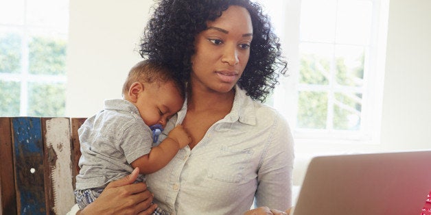 Mother With Baby Working In Office At Home Looking At Laptop