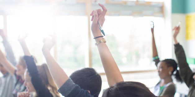 Teenage students with arms raised in classroom