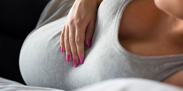 Beautiful pregnant woman relaxing and lying on the side on the bed. Holding a hand on the tummy. 