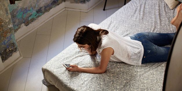 Shot of a young woman lying on her bed using a cellphone