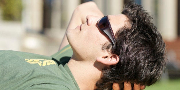 Young man resting on stack of books on lawn, side view