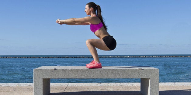 Hispanic woman doing squats on a bench by the ocean