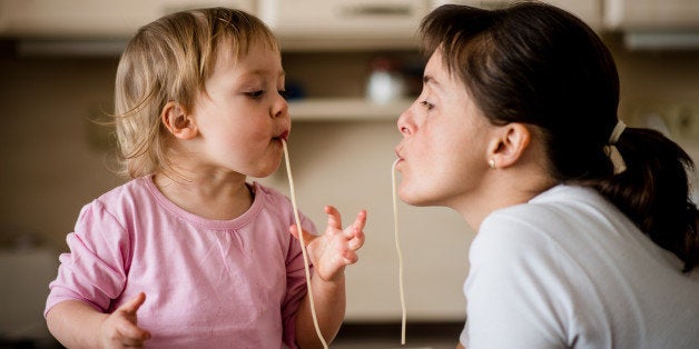 Mother and her little child sucking together spaghetti noodles.