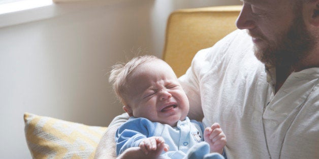 Father holding and looking at crying baby, sitting on sofa