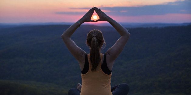 Woman meditates on a mountain top at sunset at White Rock Mountain in Arkansas.
