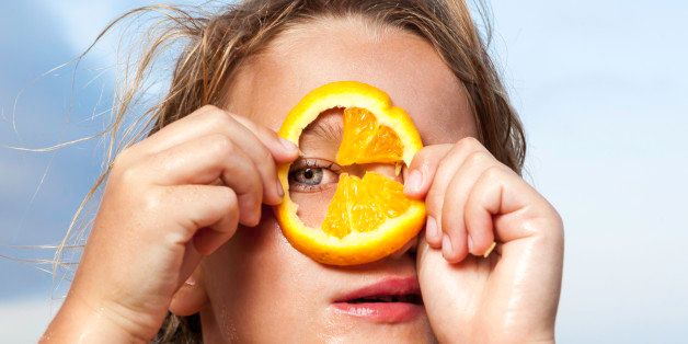 Young girl looking through slice of orange