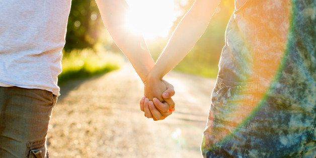 Midsection of couple holding hands on dirt road against bright sun