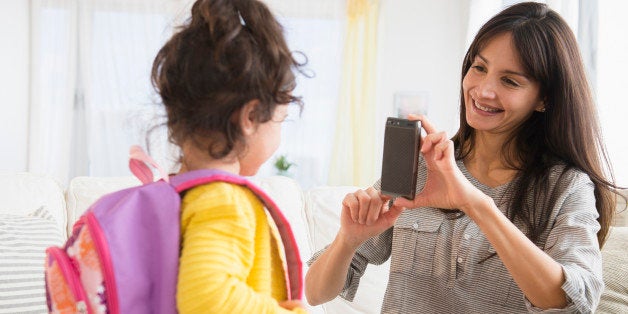 Hispanic mother taking picture of daughter ready for school