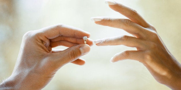 He puts a golden proposal ring on her ring-finger. The ring has a diamond.